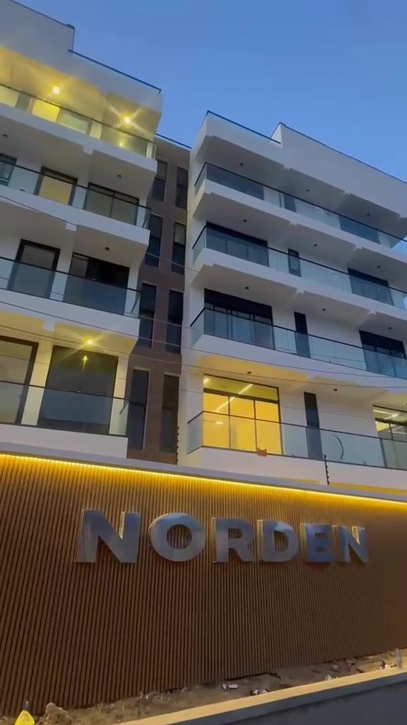 Norden Apartments at dusk, its white balconies lit above the NORDEN sign on the boundary wall