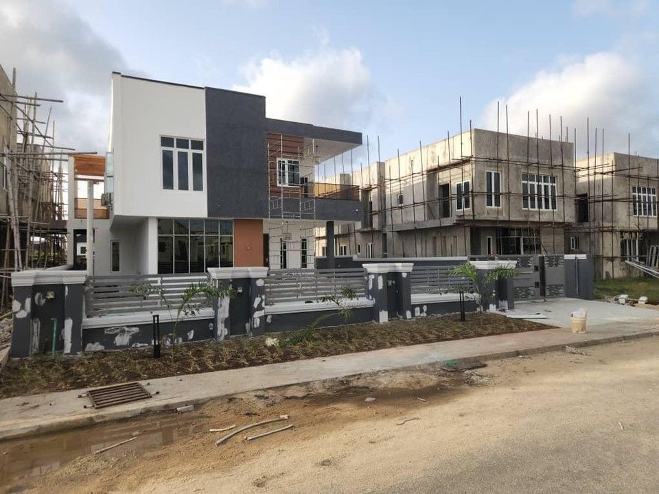 A finished two-storey duplex in grey and white at Royal Gardens Estate, with other houses under construction behind